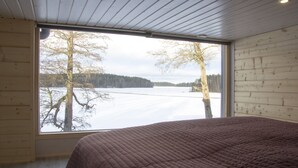 Makuuhuoneessa on suuri ikkuna, puuseinät ja sänky, jossa on ruskea peitto.