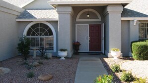A residential house with a red door, a large arched window, and a small garden with gravel and plants. - Private Heated Pool & Spa - Putting Green - Huge Back Yard - Great Location  (Chandler)