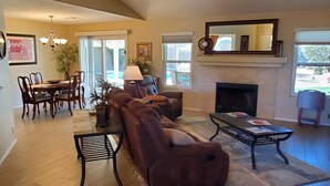 A spacious living room with a fireplace, a dining area with a table and chairs, and a large window providing natural light. - Private Heated Pool & Spa - Putting Green - Huge Back Yard - Great Location  (Chandler)