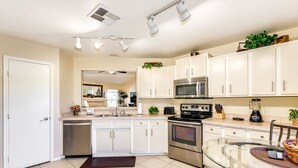 A modern kitchen with white cabinets, stainless steel appliances, and a glass dining table. - Private Heated Pool & Spa - Putting Green - Huge Back Yard - Great Location  (Chandler)