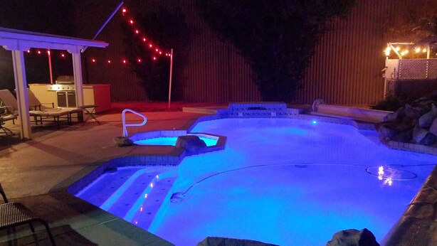 A swimming pool with a hot tub, surrounded by rocks and a pergola with string lights. - Private Heated Pool & Spa - Putting Green - Huge Back Yard - Great Location  (Chandler)