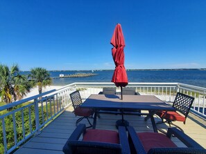 Um terraço com mesa e cadeiras, um guarda-sol vermelho e vista para a água.