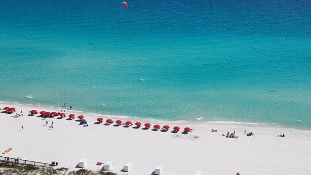 Une plage de sable blanc, parsemée de parasols rouges, et une mer d’un bleu limpide.