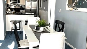 Una cocina compacta con electrodomésticos modernos, un comedor con mesa y sillas blancas, y un espejo grande en la pared.