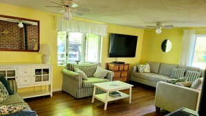 A living room with a striped sofa, a grey sofa, a coffee table, a TV, and a ceiling fan.