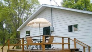 A wooden deck with a table and chairs, a covered umbrella, and a house in the background.