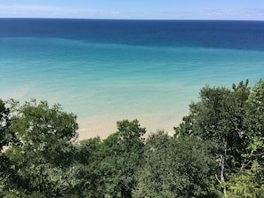 A coastal view with clear turquoise waters, a sandy beach, and dense green foliage in the foreground. - Pet Friendly - No Cleaning Fee - Centrally Located Within Lower Northwest Mich. (copemish)