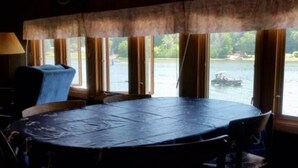 A dining area with a round table and chairs, large windows overlooking a body of water with a boat visible. - 3 Bedroom Cottage on Long Lake (Hastings)