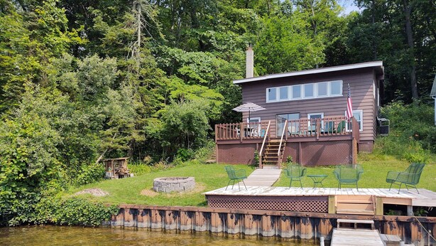 A cabin with a deck, a fire pit, and a dock extending into a lake. - 3 Bedroom Cottage on Long Lake (Hastings)