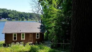 A small cabin by a lake with a wooden deck and a single door. - 3 Bedroom Cottage on Long Lake (Hastings)
