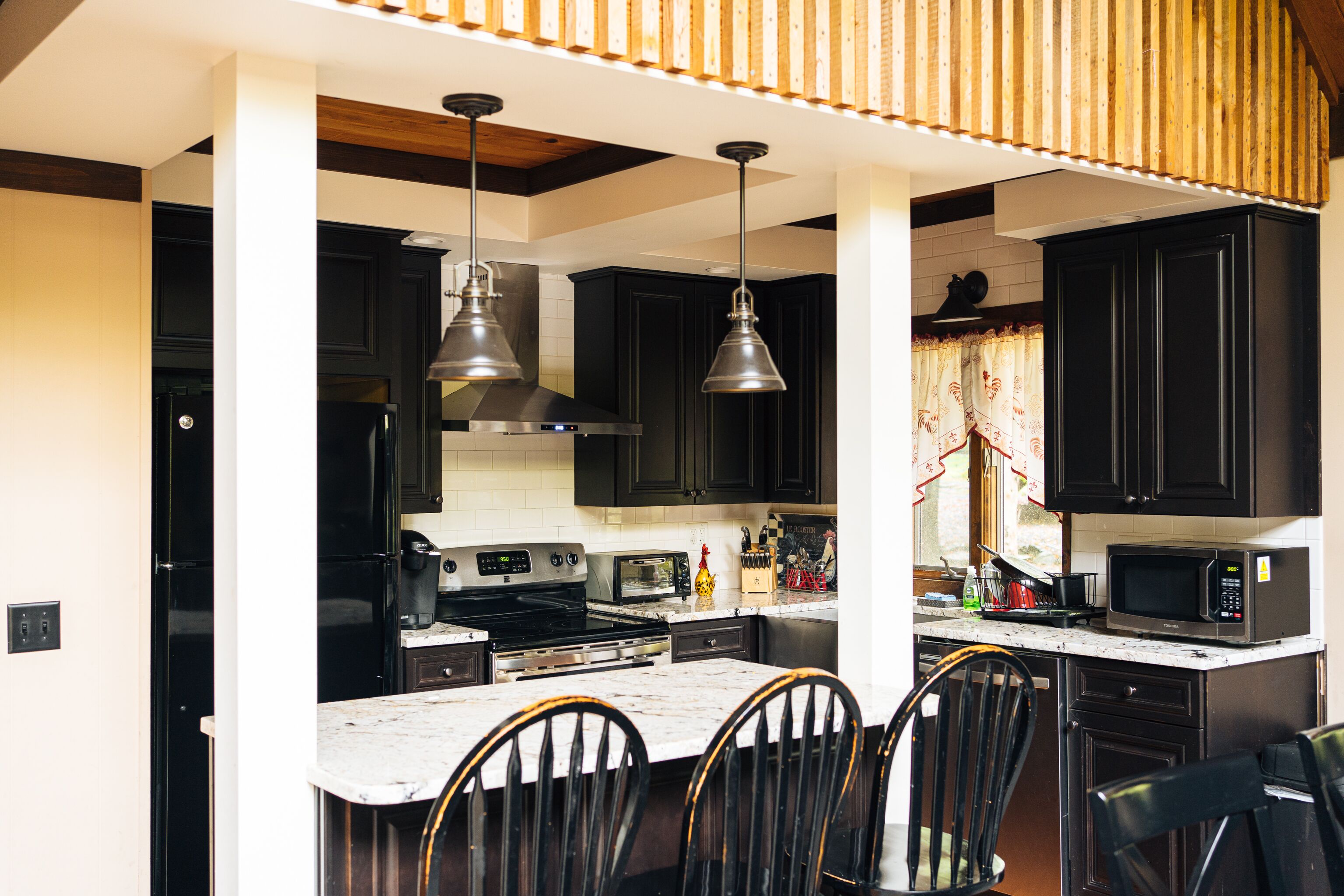 A kitchen with black cabinets, a white countertop, and a central island with chairs.