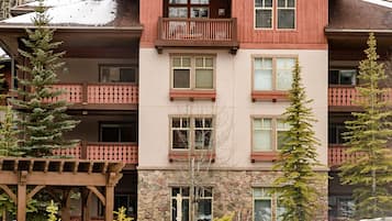 A multi-story building with a red and beige facade, balconies, and a stone base.