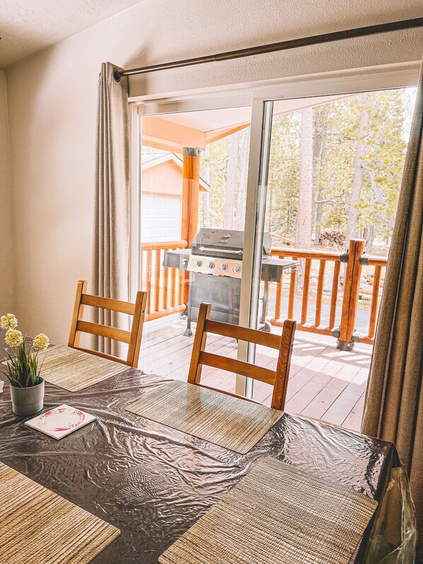 A dining area with a table, chairs, and a view of a barbecue grill outside.