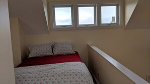 A bedroom with a bed, two pillows, a red blanket, and a window with a view of the sky. - 2 Bedroom, second row beach cottage .  (Cedar Island)