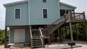 A two-story house with a wooden deck and a staircase leading to a balcony. - 2 Bedroom, second row beach cottage .  (Cedar Island)