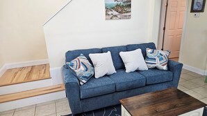 A living room with a blue sofa, patterned pillows, a wooden coffee table, and a rug with a whale design. - 2 Bedroom, second row beach cottage .  (Cedar Island)
