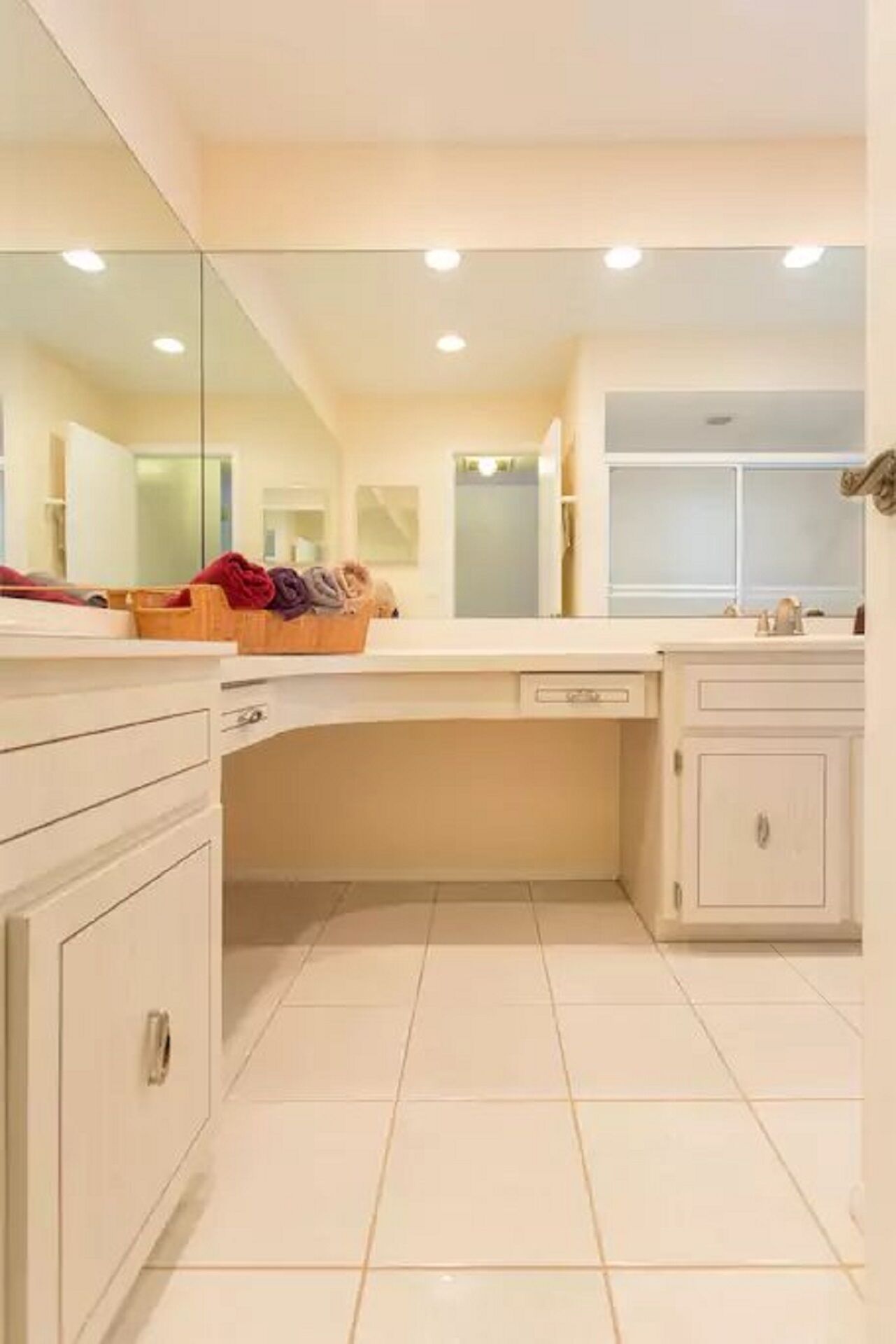 A modern bathroom with a large mirror, white cabinetry, and a tiled floor.