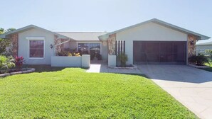 A modern two-story house with a garage, a well-maintained lawn, and a stone accent wall. - Waterfront Home With Pool (Port Richey)