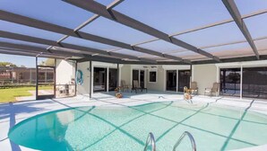 A covered swimming pool with clear water, surrounded by a patio area with chairs and a hose. - Waterfront Home With Pool (Port Richey)