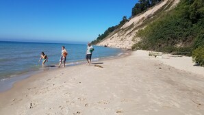 Una playa arenosa con cielo azul despejado y un promontorio rocoso al fondo.