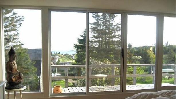 Une pièce dotée d’une grande porte-fenêtre coulissante donnant sur un balcon avec vue sur un paysage verdoyant et une étendue d’eau.