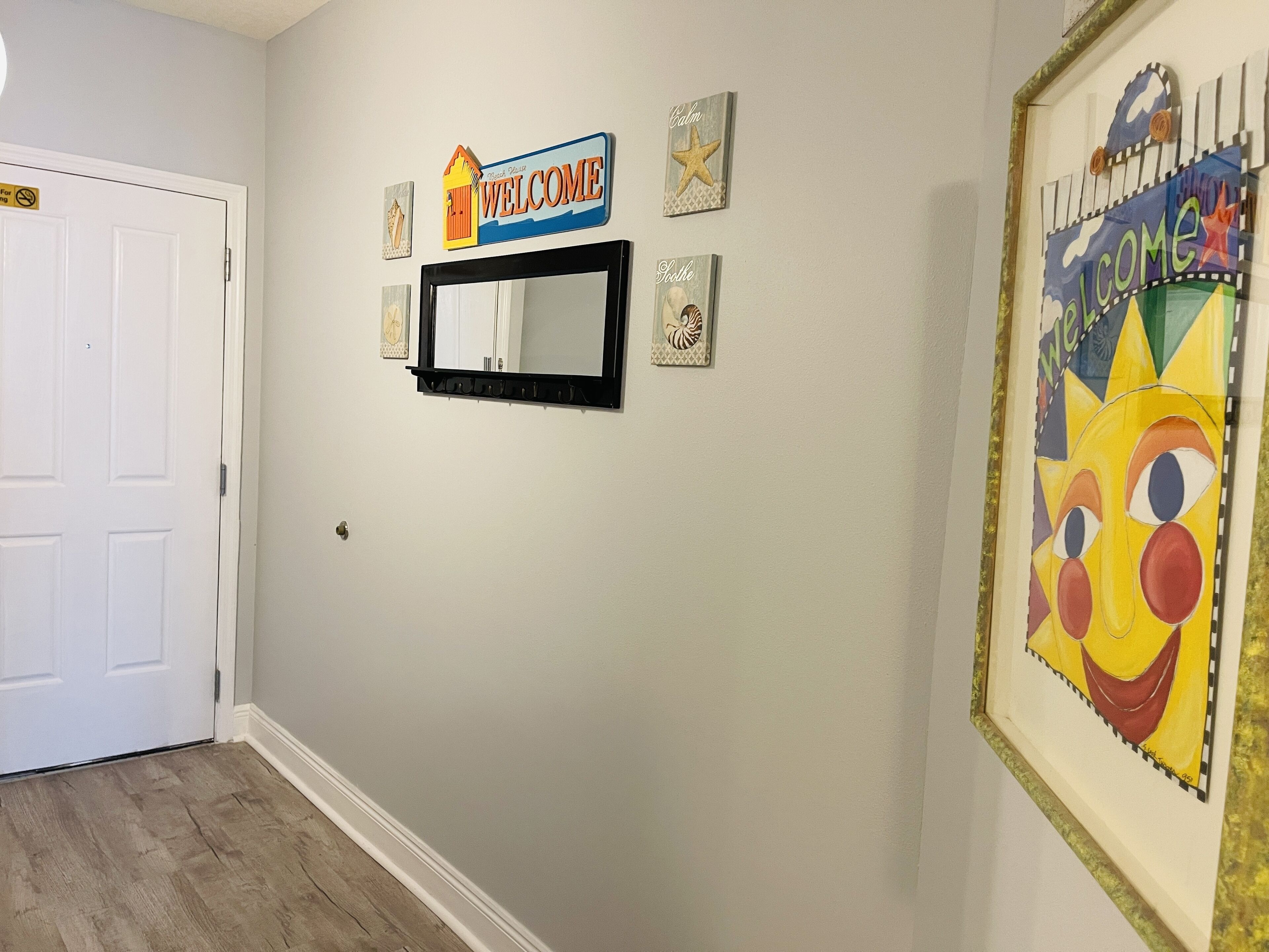 A hallway with a welcome sign, a mirror, and a framed artwork.