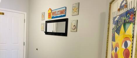 A hallway with a welcome sign, a mirror, and a framed artwork.