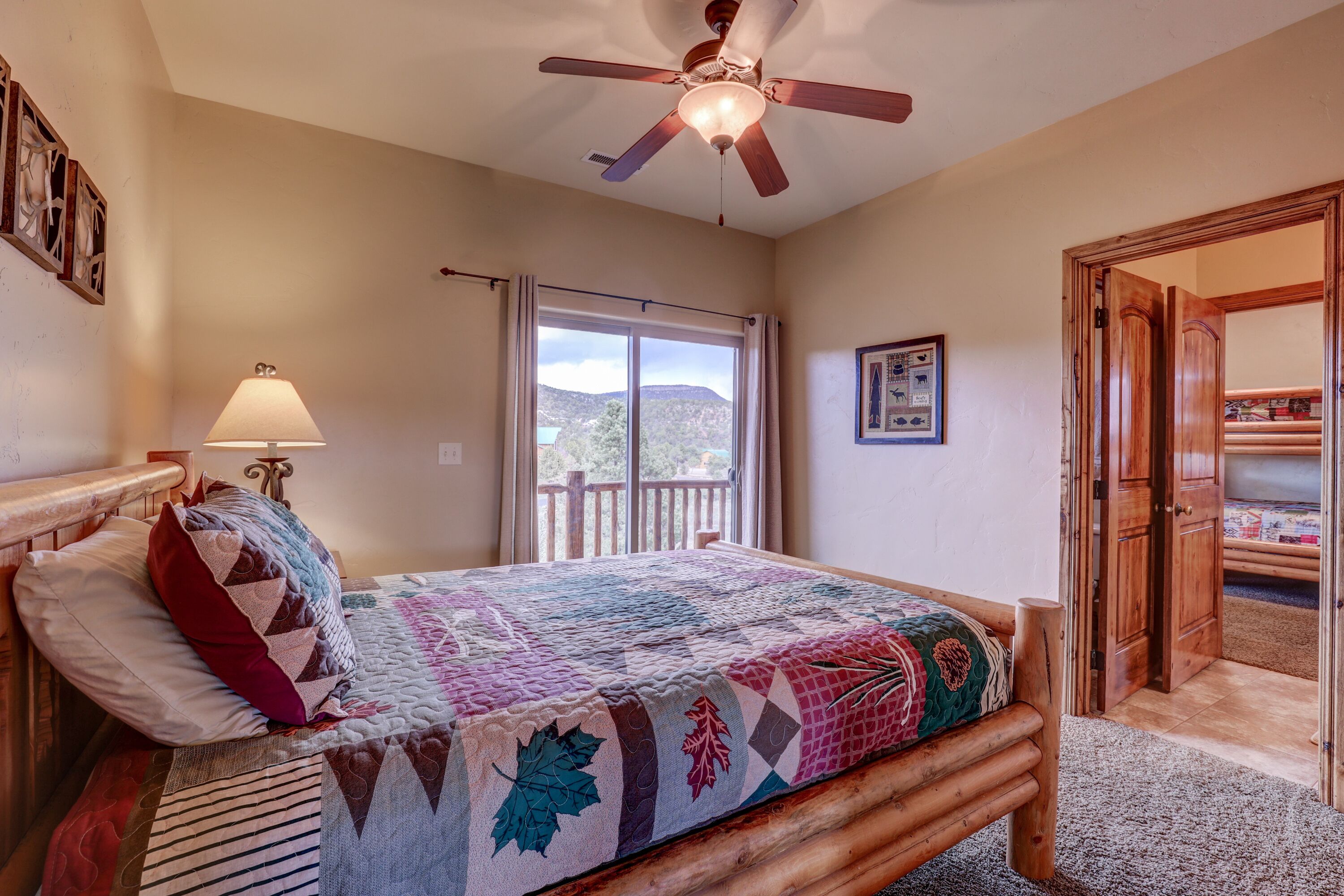 A bedroom with a wooden bed, a ceiling fan, a window with a view, and a door leading to another room.