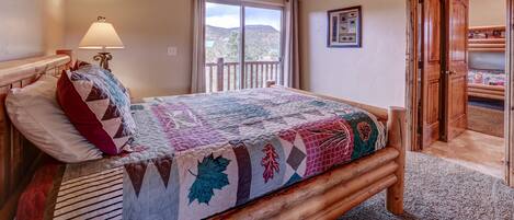 A bedroom with a wooden bed, a ceiling fan, a window with a view, and a door leading to another room.