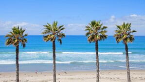 Une plage avec quatre palmiers et l’océan en arrière-plan.