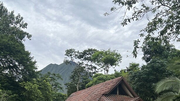 Una casa con techo de tejas, rodeada de abundante vegetación y una montaña al fondo.