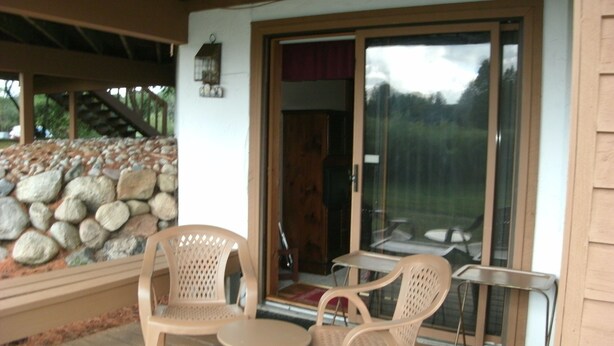 A covered patio with two plastic chairs and a small table, a stone wall, and a sliding glass door leading to an interior space.