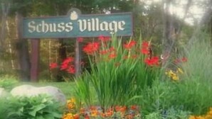 A sign for 'Schuss Village' surrounded by a garden with various flowers.