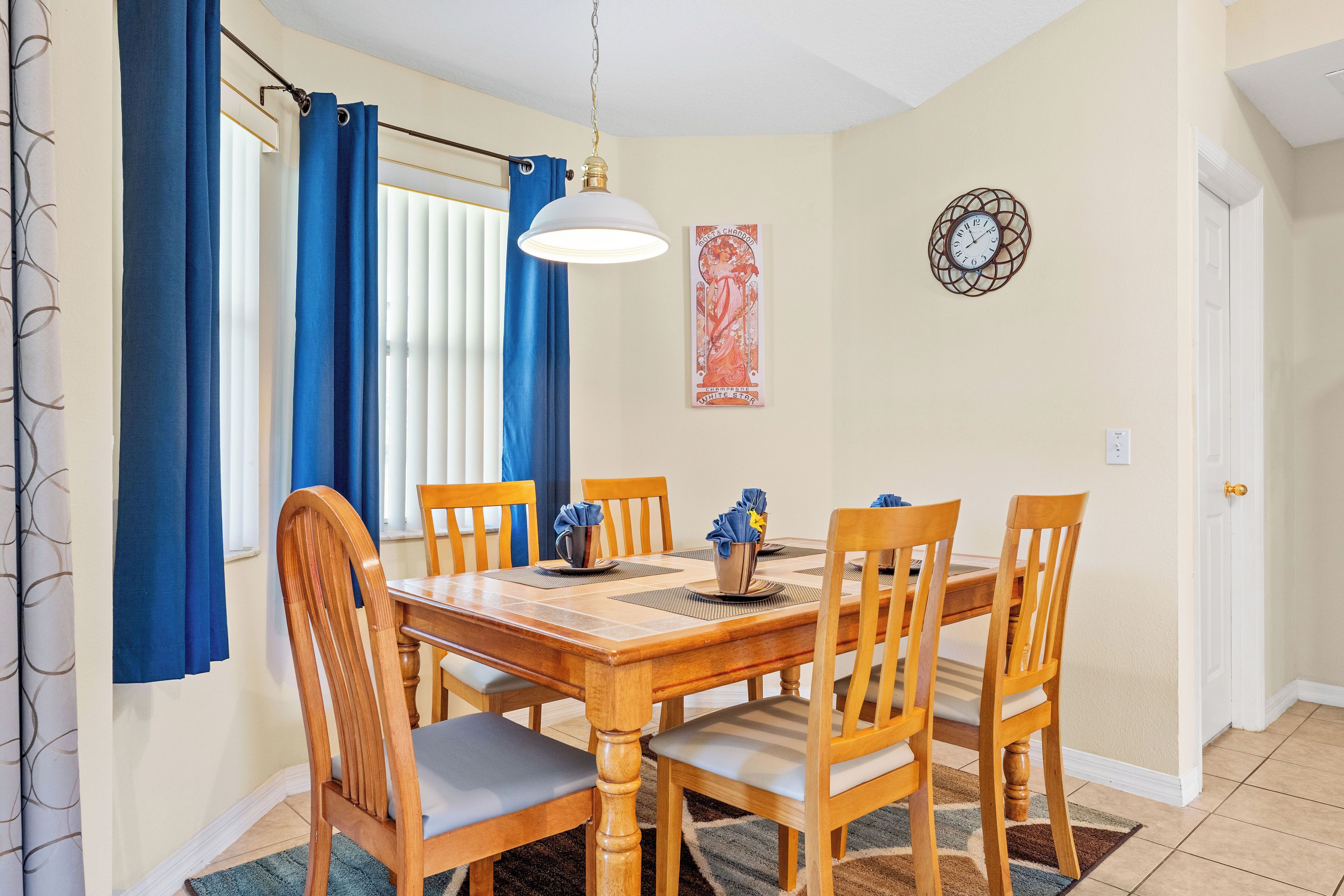 A dining area with a wooden table, six chairs, and a hanging light fixture.