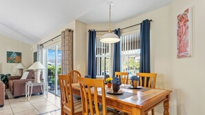 A dining area with a wooden table and chairs, a chandelier, and a view through large windows with blue curtains. - Last-Minute-Rates  . LET YOUR DREAMS COME TRUE - King Bed, Gas Grill & Game Room (Davenport)