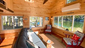 Ein gemütliches Blockhausschlafzimmer mit Sofa, Sesseln und großen Fenstern mit Seeblick.