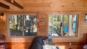 Ein gemütliches Blockhaus-Interieur mit einem großen Fenster, das Blick auf einen Wald und einen See bietet.