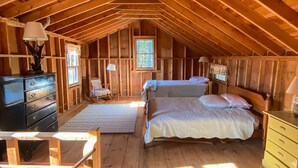 Ein gemütliches Schlafzimmer im Dachgeschoss mit Holzbalkendecke, einem Bett, einer Kommode und einem Fenster.