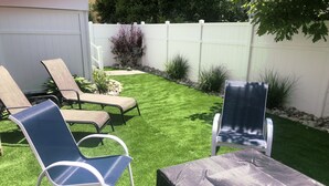 A backyard with artificial grass, a white fence, and outdoor furniture including two lounge chairs and a table. - Almost Beachfront, 7 houses to the Beach (Ventnor City)