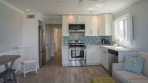 Une cuisine avec des armoires blanches, des appareils en acier inoxydable, un dosseret en motif chevrons et un ventilateur de plafond.
