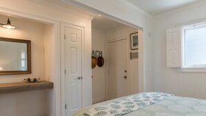 Une chambre à coucher comprenant un lit, une commode, un miroir et une porte donnant sur une salle de bain.