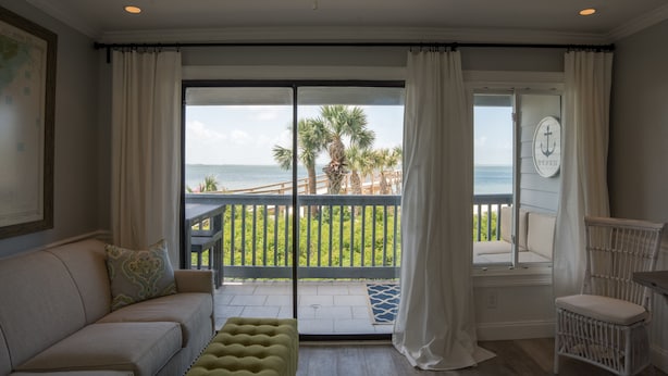 Une chambre avec un balcon donnant sur l’océan, un canapé, un fauteuil et une petite table.