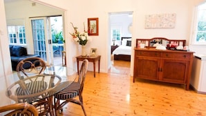Una habitación con una mesa de comedor de vidrio, sillas de mimbre, un armario de madera y una cama con ropa de cama blanca.