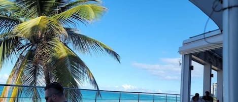 A man relaxing on a white lounge chair with a view of the ocean and a palm tree.