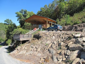 Situated on a rocky hillside, this cabin features a covered porch and a wooden deck with a railing.