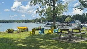 A lakeside picnic area with a wooden table and colorful Adirondack chairs. - Herons Nest at Viewpoint Beach channel on Magician Lake, Sister Lakes, MI 49047 (Sister Lakes)