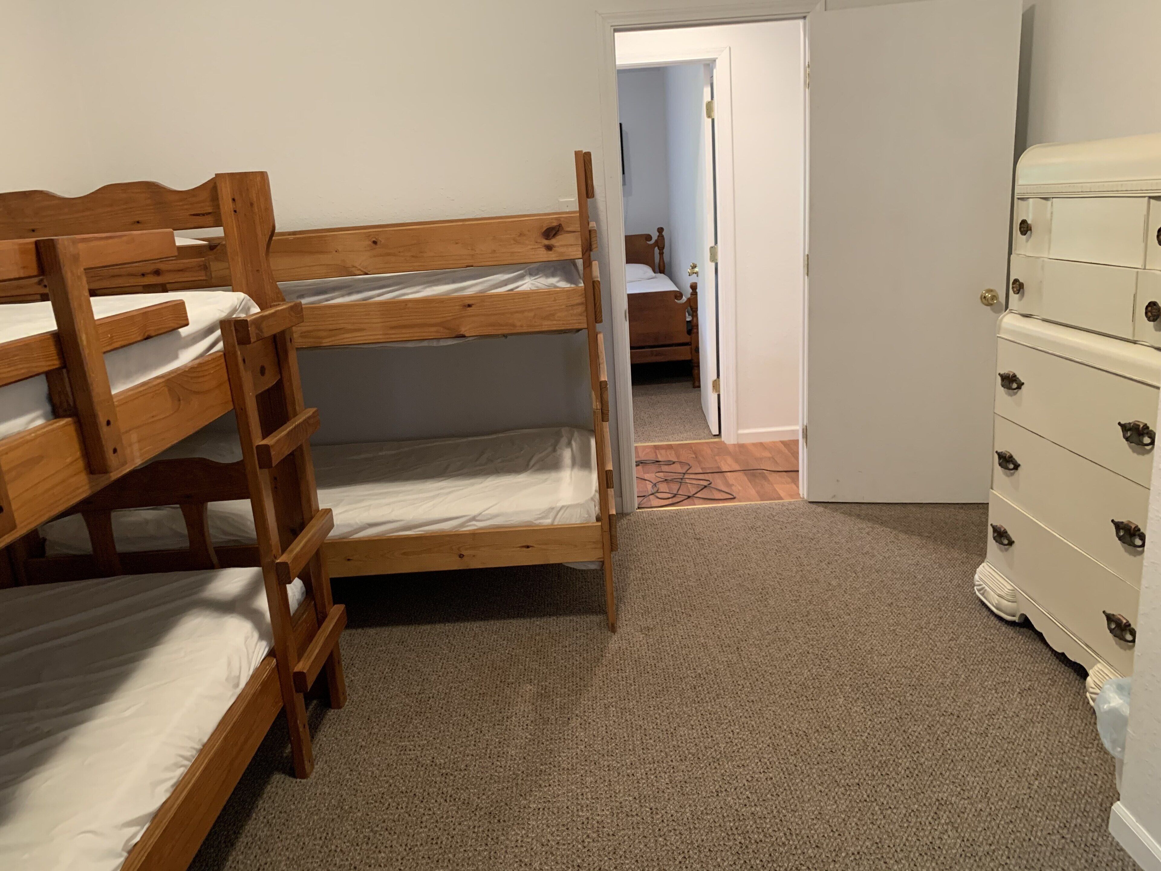 Une chambre avec un lit superposé, une commode et une porte donnant sur une autre pièce.
