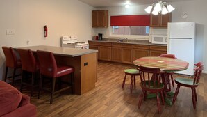 A kitchen with wooden cabinets, a stove, a microwave, and a refrigerator. There is a dining area with a table and chairs. - Herons Nest at Viewpoint Beach channel on Magician Lake, Sister Lakes, MI 49047 (Sister Lakes)