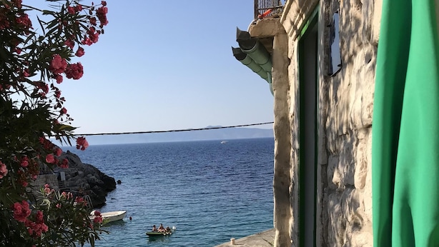 Eine Terrasse am Meer mit einem weißen Tisch, Blumentöpfen und Blick aufs Meer.