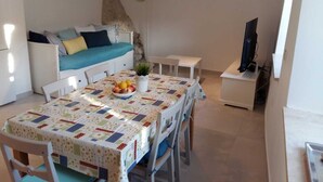 Ein gemütlicher Wohnbereich mit einer Couch, einem Esstisch mit einer Patchworkdecke, einer kleinen Pflanze und einem Fernseher.